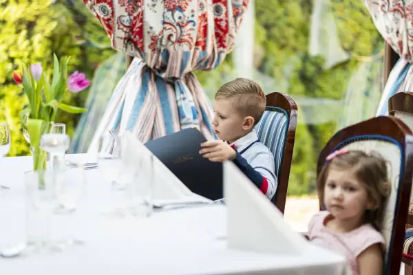 Chłopiec przy weselnym stole dla dzieci przegląda menu. Obok siedzi dziewczynka.